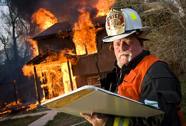 A firefighter chief stands before a residential structure fire holding an accountability chart with copy-space.