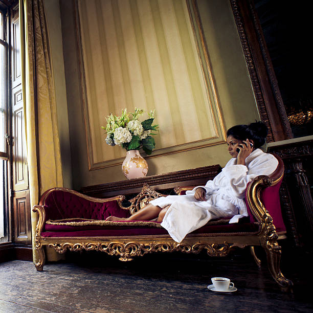 Young female in bathrobe, sitting on red couch and talking on the phone.