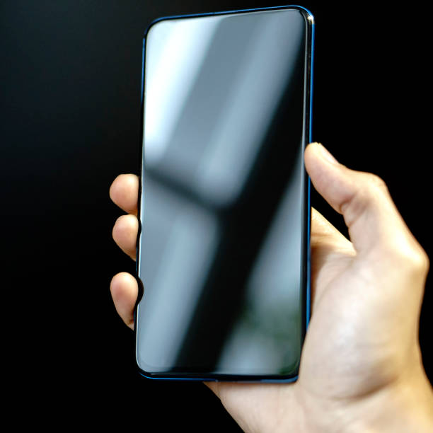 istock Male hand holding a smartphone. Mobile phone network connection and communication on black background. 1171452156