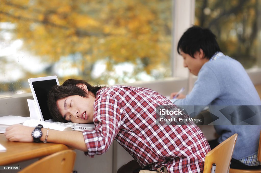 Two Asian students studying but one has fallen asleep College Student sleeping on his laptop when he should be studying. iStockalypse Tokyo 2010. Sleeping Stock Photo