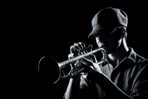 Black and white, high contrast image of a young man playing on a trumpet.