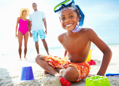 Boy sitting on the beach with parents in the background