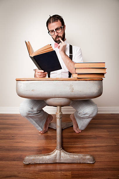 The image shows a man with a beard reading a book while wearing a formal vest and tie, lit dramatically.