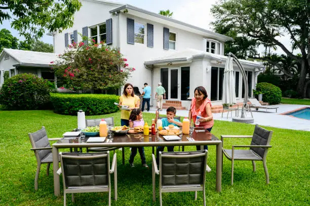 Three generations of Hispanic family members cooking and preparing the table for an outdoor barbecue lunch.