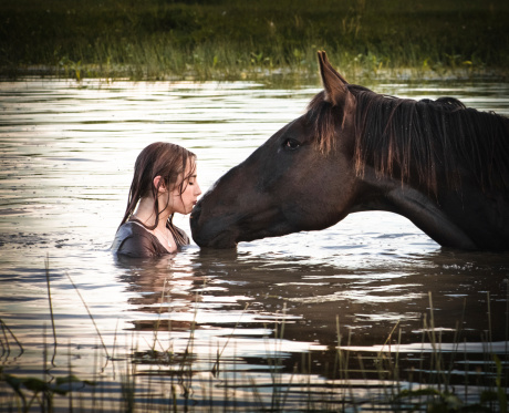 Teen girl kissing her horse in the water pond.
