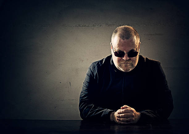 mafia member mean fellow pretending to be an irish mobster - he is seating by an empty table and stares at camera wearing sunglasses mafia boss stock pictures, royalty-free photos & images