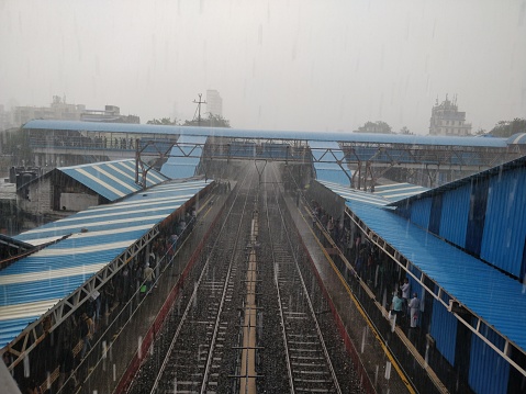 Mumbai, India - July 28, 2019: Crowd boarding train in Mumbai railway station under heavy monsoon rain