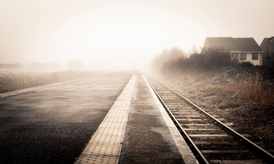 Railway platform in the middle of nowhere on a foggy day. Yellow toned picture and desaturated colour for the mood.