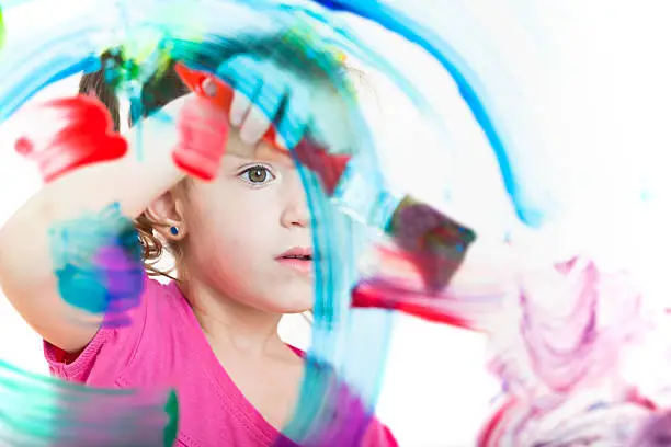 Photo of Blonde little girl painting with colours on window