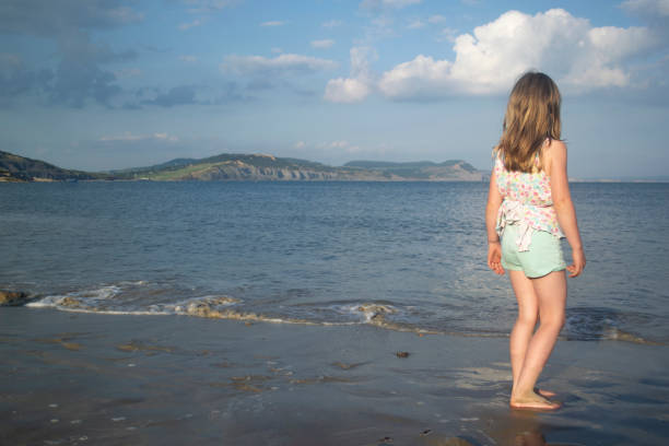 Young woman enjoying the soothing waves as they wash over her feet at the sandy beach, embracing the warmth of a sunny summer day