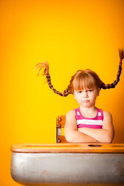 頑固なレッドヘア子羊の女の子が学校デスクで腕を組む - anger child braids braided ストックフォトと画像