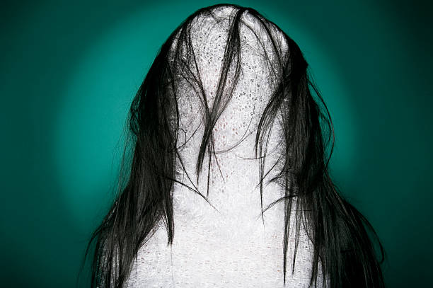 A woman with long hair poses gracefully in a black outfit, exuding confidence and elegance in a simple studio environment.