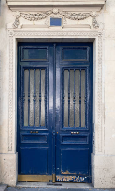 istock Doorway with door windows with matte glass protected by vertical patterned grids. Dark blue painted antique door with shabby bottom part. Antique building in Paris France. Exterior of house in Europe 1171478539