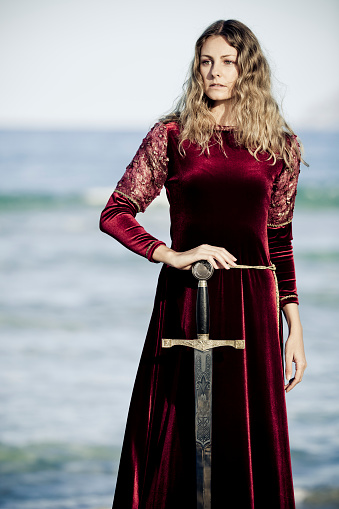 portrait of medieval lady in flashy satin dress guarding the kings sword for novel concepts,selective focus, creative dramatic color retouching to underline the ancient medieval time,vignetting 