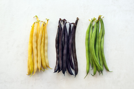Green, yellow and purple string beans on white background.