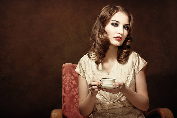 Pretty young woman relaxing with a cup of coffee. Nostalgic retro style, toned image, added real film grain, vignette. Original clothes and other accessories from the first part of the XX. century.