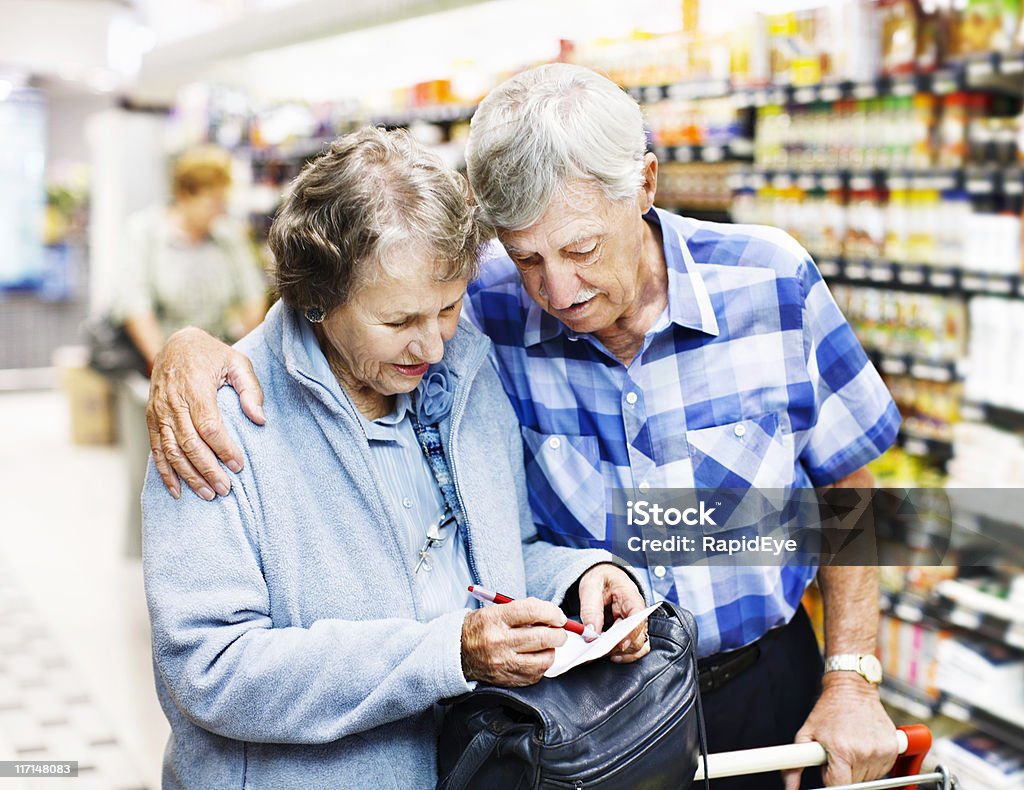 Affettuoso Coppia senior controllare Lista della spesa nel supermercato - Foto stock royalty-free di Coppia anziana