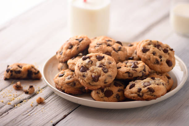 Pile of Delicious Chocolate Chip Cookies on a White Plate with Milk Bottles stock photo