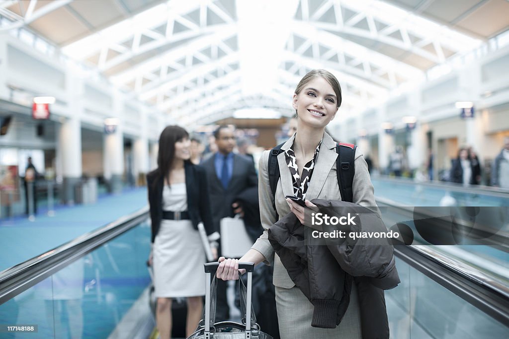 Aeropuerto de un pasillo mecánico con sonriente empresaria sosteniendo célula, espacio de copia - Foto de stock de Ejecutiva libre de derechos