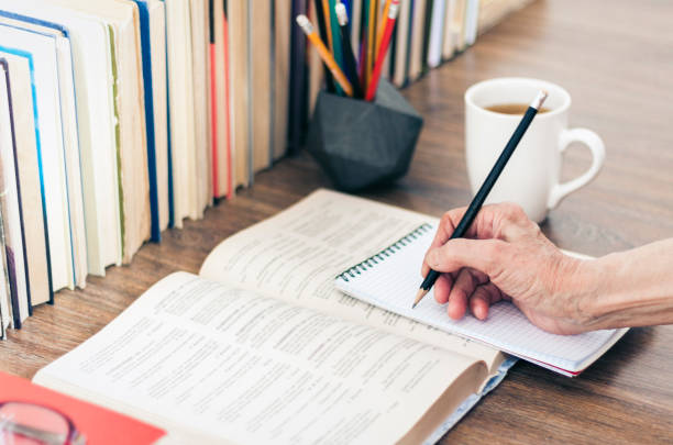 istock Stack of books education background, female hand makes notes in open notebook. Glasses, pens and pencils in holder, cup of tea with lemon 1171482317