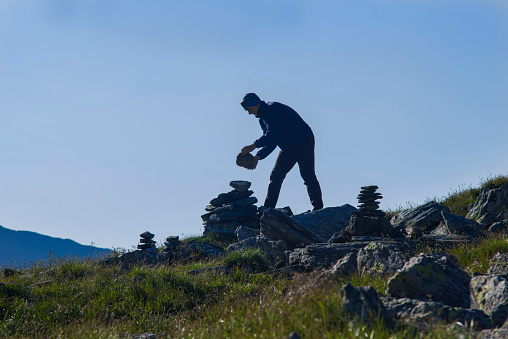 Stone pile mark in mountains. Man adding a stone to the pile.