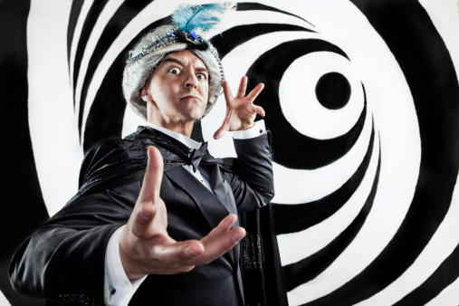 A stock photo of a Hypnotist inducing a trance and gesturing on a black and white swirl background.
