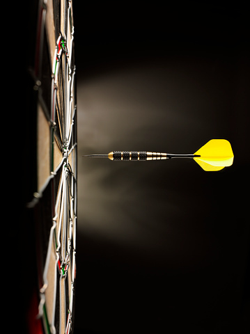 One yellow darts hitting the target in a game of darts scoring a bulls eye.  Copy space