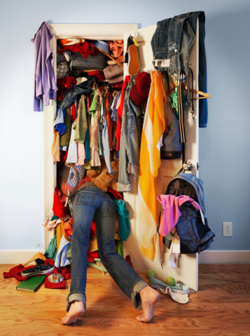 Young woman diving into her very messy, unorganized closet searching for something. Vertical shot.