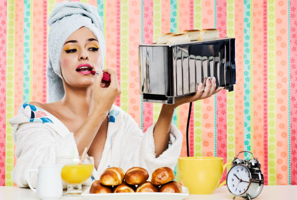 Gorgeous woman's, breakfast lipstick and toaster. One beautiful woman having breakfast, she is using a shiny toaster as a mirror and putting some lipstick on. She is wearing a bathrobe and has her hair wrapped in a towel. Colorful background and horizontal format. Concept young adult lifestyle and body care. diva human role stock pictures, royalty-free photos & images