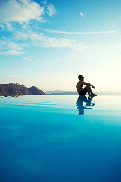 High angle view from the edge of an infinity swimming pool. Blue variation of sky and sea. Reflection on water surface with wavy pattern. Poster background with large copy space. Relaxing summer vacation escape.