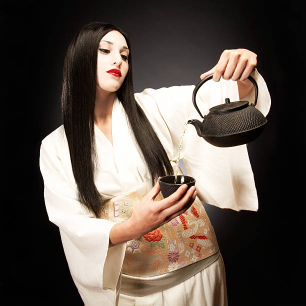 Beautiful Dark Haired Young Woman Dressed as Geisha Pouring Tea stock photo