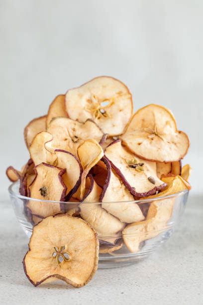 istock Hipped Dried apples chips in glass bowl on light background, vertical composition, vetical composition 1171489717
