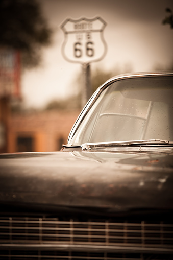 A rusty vintage 1960's-era American car sits rusting next to a Route 66 sign somewhere in Arizona
