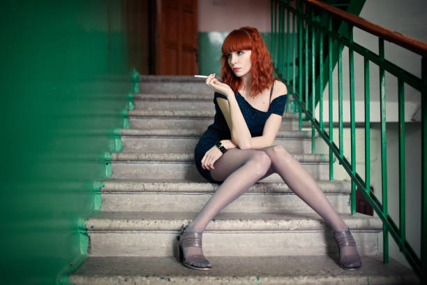 Vulgar redhead girl sitting on the stairs and smokes stock photo