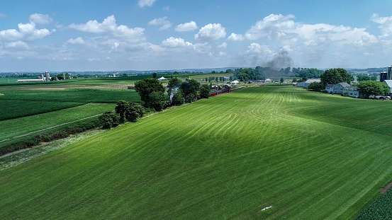 An Aerial View of a Steam Train Arriving in Amish Countryside on a Summer Day as Seen by a Drone