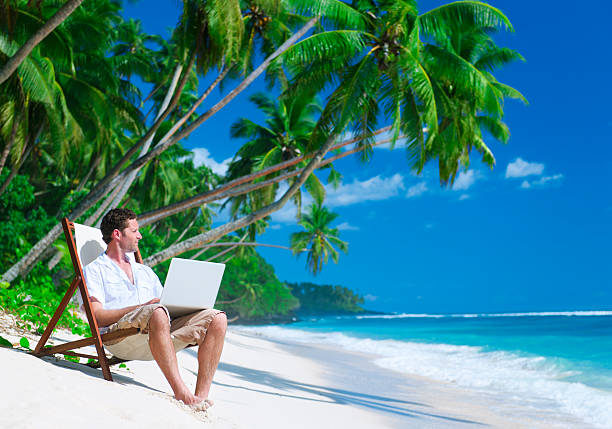 istock Man with laptop relaxing under palm tree on white sand beach 117149509