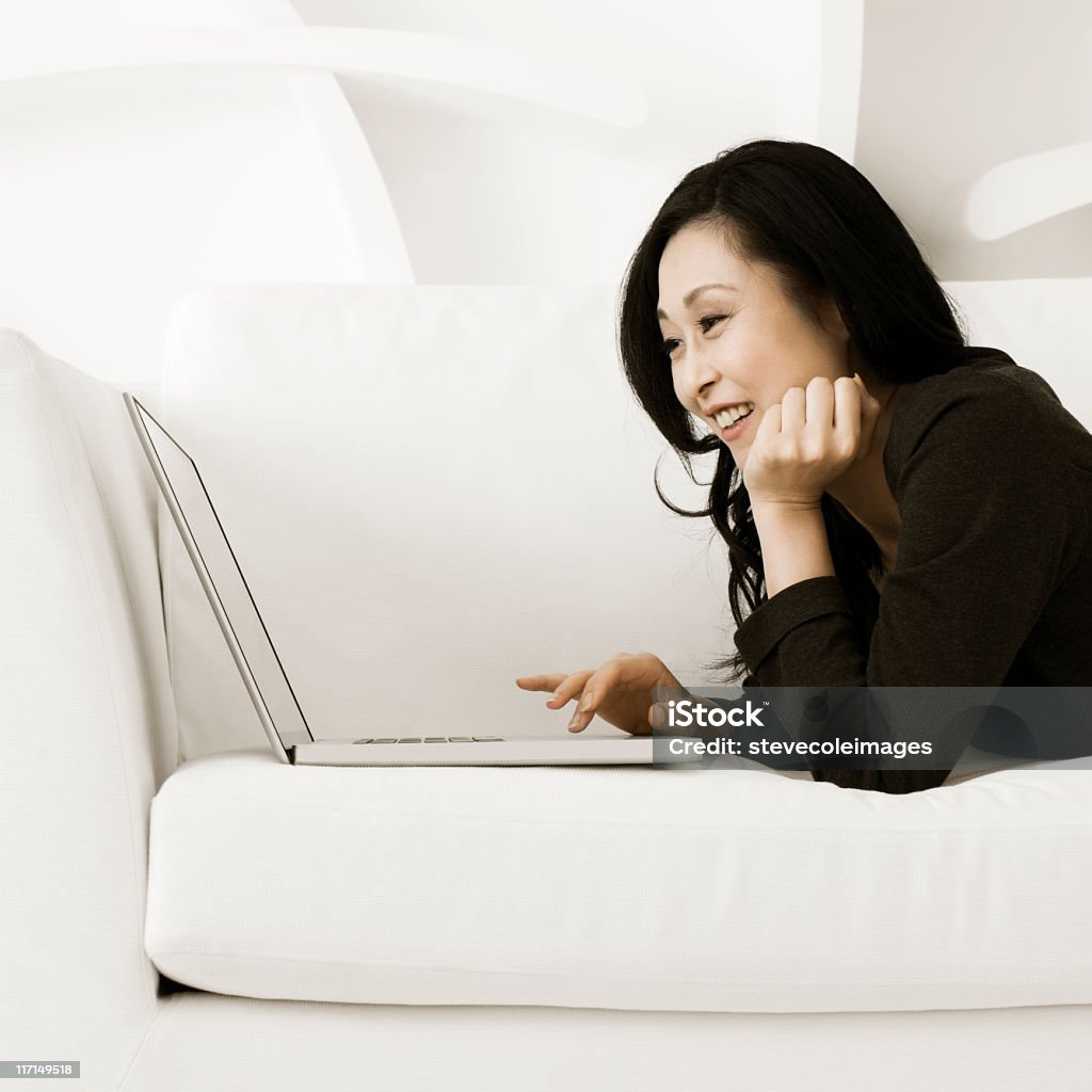 Женщина, лежа на диване и используя ноутбук - Стоковые фото 40-49 лет роялти-фри