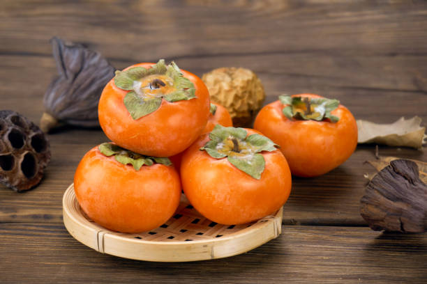 istock fresh ripe persimmons isolated on wood background 1171495382