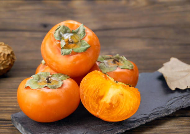 istock fresh ripe persimmons isolated on wood background 1171495390