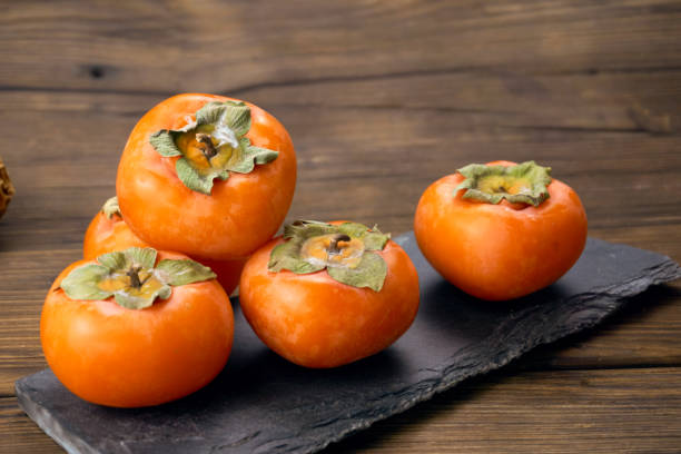 istock fresh ripe persimmons isolated on wood background 1171495391