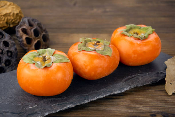 istock fresh ripe persimmons isolated on wood background 1171495517