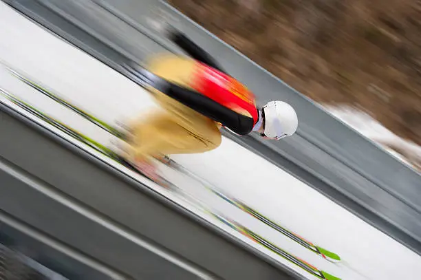 Side view of young male ski jumper in the inrun section of the ski jump, speed 45 MPH, motion blurred, diagonal composition