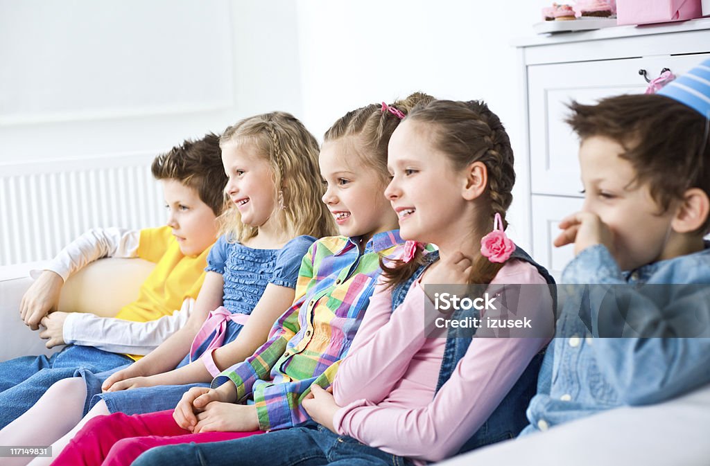 Children watching TV Side view on five smiling kids sitting in a row on sofa in domestic room, watching TV and smiling. Selective focus. Children Only Stock Photo