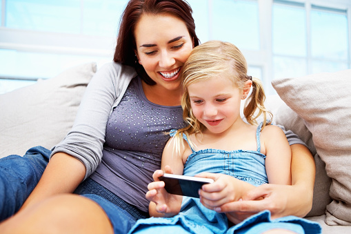 Young mother and daughter using a cell phone while sitting on a couch