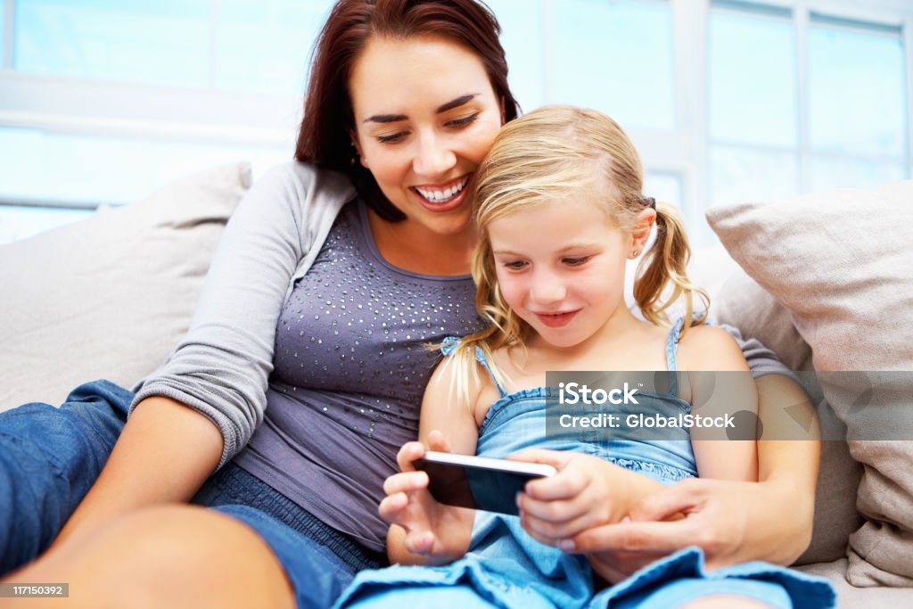 Mother and daughter using a cell phone on couch Young mother and daughter using a cell phone while sitting on a couch 20-29 Years Stock Photo