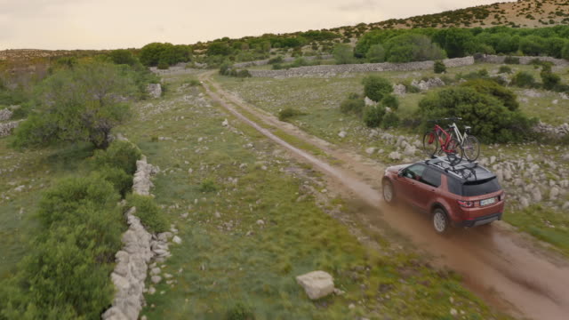 Drone shot of an offroad car splashing through a puddle while driving on a gravel road somewhere on a remote location on the Krk Island. Croatia. Europe