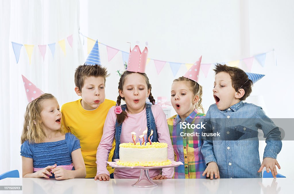 Blowing out birthday candles Portrait of five cute, kids wearing party hats having fun at birthday party. Standing at the table and blowing out birthday candles. Party - Social Event Stock Photo