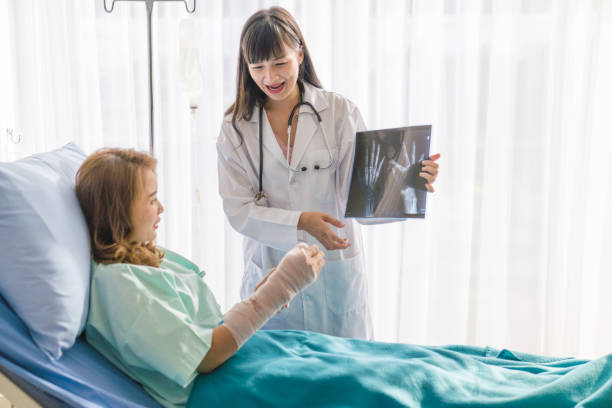professionelle ärzte interpretieren röntgenbild zu weiblich falten gebrochenen arm mit bandage der hand, während patient sitzen auf rollstuhl im krankenhaus - singapore mrt stock-fotos und bilder