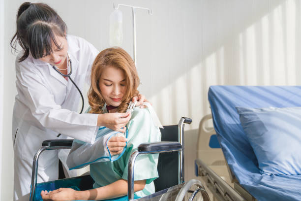 professionelle ärzte interpretieren röntgenbild zu weiblich falten gebrochenen arm mit bandage der hand, während patient sitzen auf rollstuhl im krankenhaus - singapore mrt stock-fotos und bilder