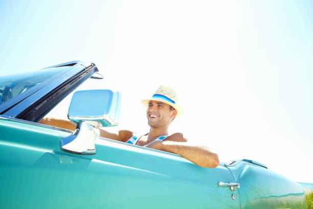 istock Smiling young man wearing hat while driving convertible car 117150759